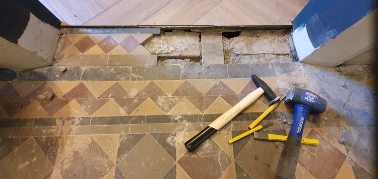 Worker examining the subfloor condition beneath Victorian tiles for dampness and damage